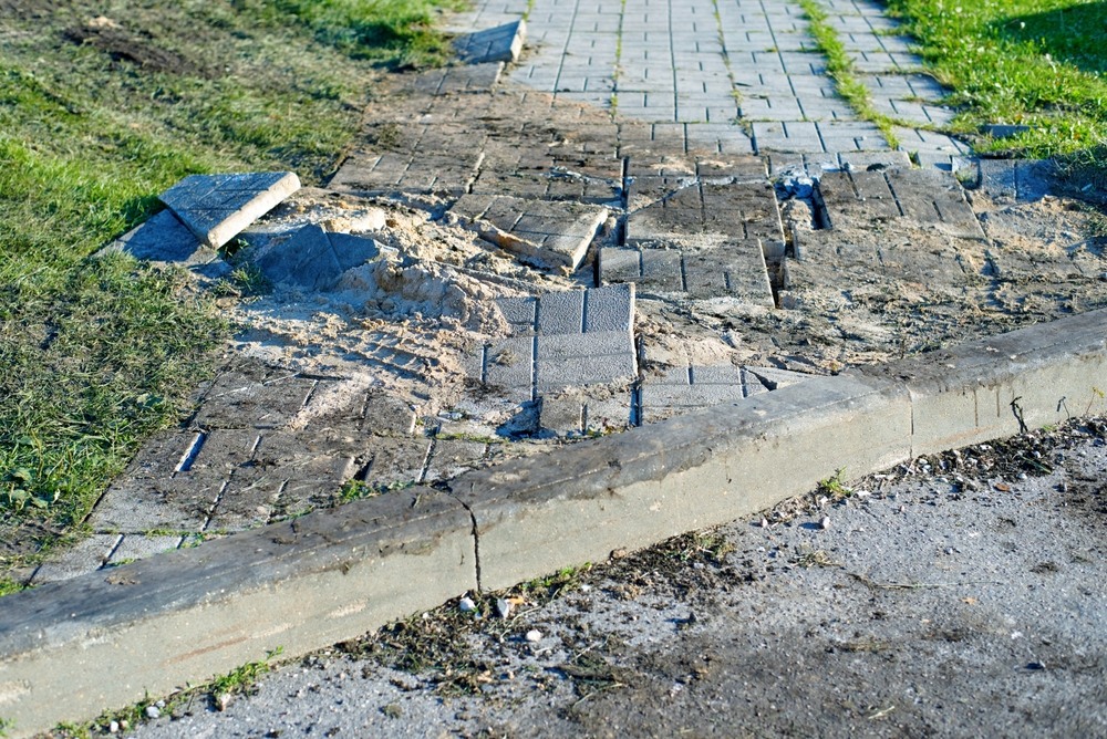 Cracked and uneven sidewalk pavers with a raised edge, a common trip hazard in unsafe sidewalk injury claims