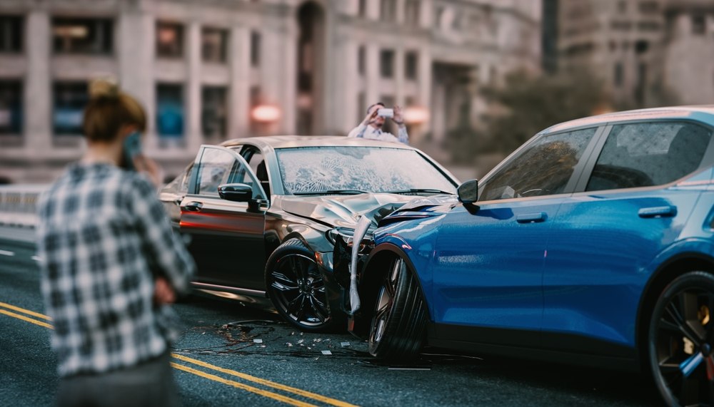 Person on the phone and another photographing a multi-vehicle car accident scene on a city street, illustrating evidence documentation after a Newark crash