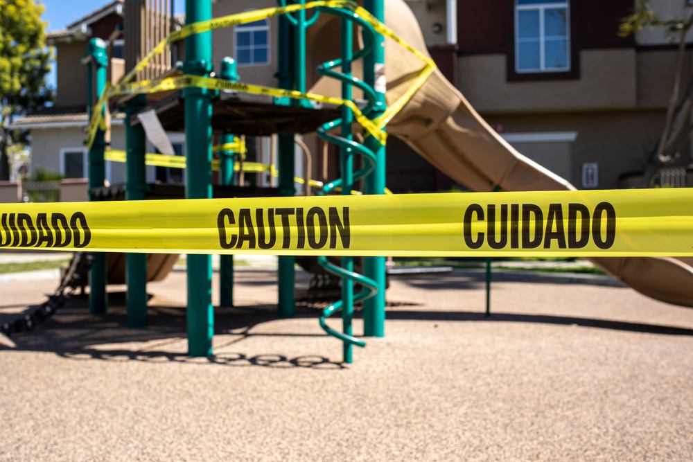 Yellow caution and cuidado tape wrapped around playground equipment, illustrating a hazardous condition relevant to premises liability claims