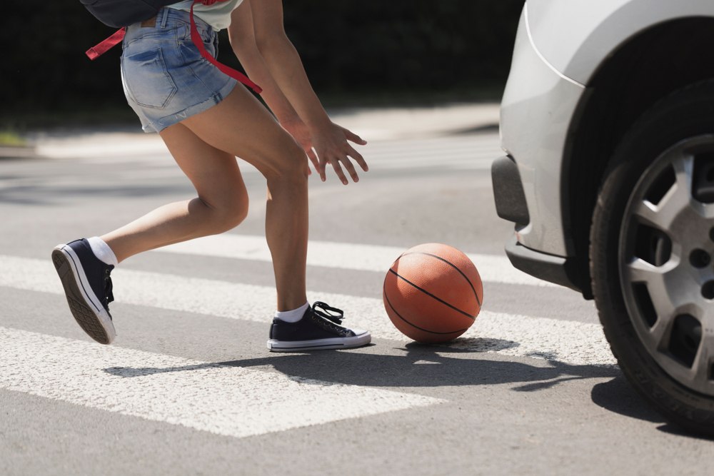 Child running across a marked crosswalk after a basketball rolls into the street near an oncoming car