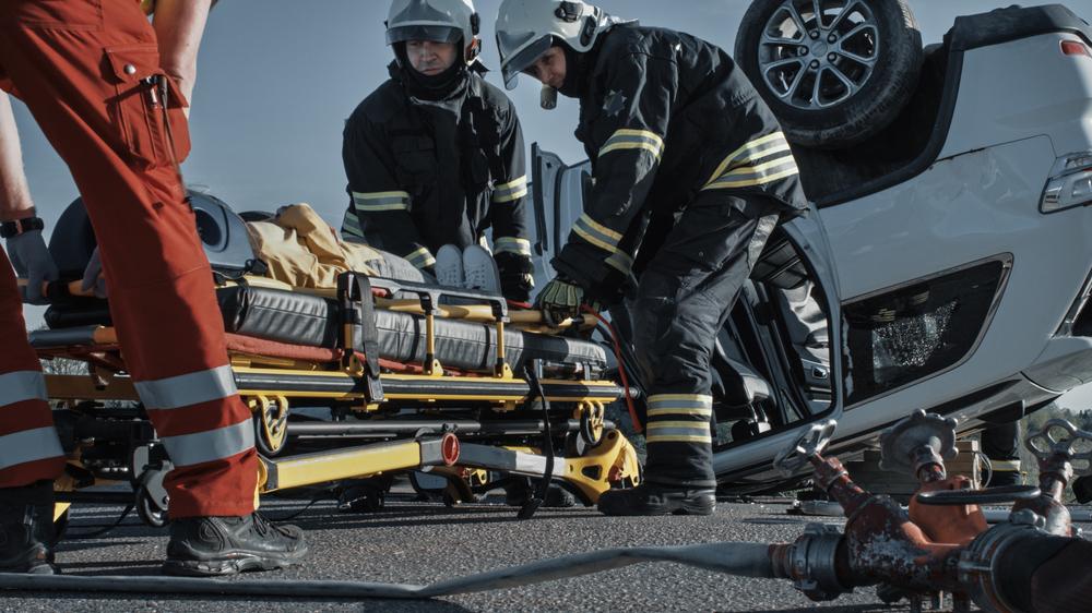 Firefighters and paramedics preparing a stretcher beside an overturned vehicle, illustrating emergency response to a catastrophic car accident injury