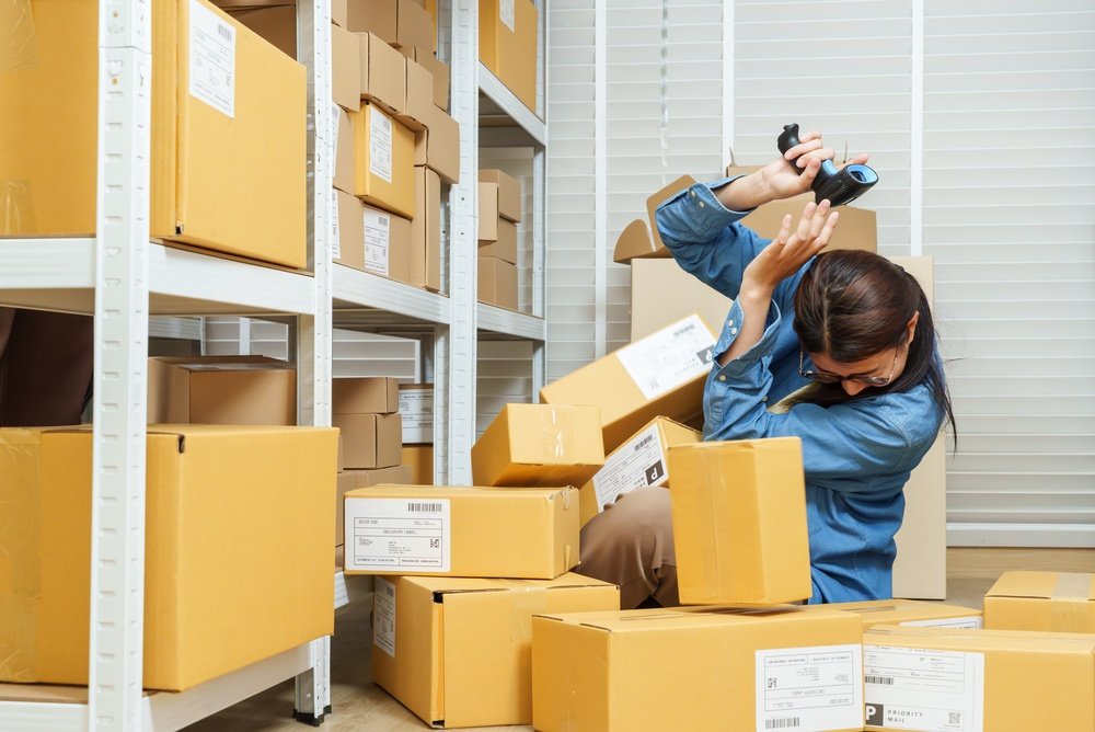 Worker covering her head as boxes fall from a warehouse shelf in a retail stockroom