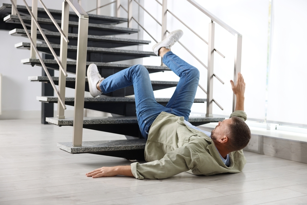 Man falling backward down an indoor staircase, reaching for a handrail during a stairway fall accident