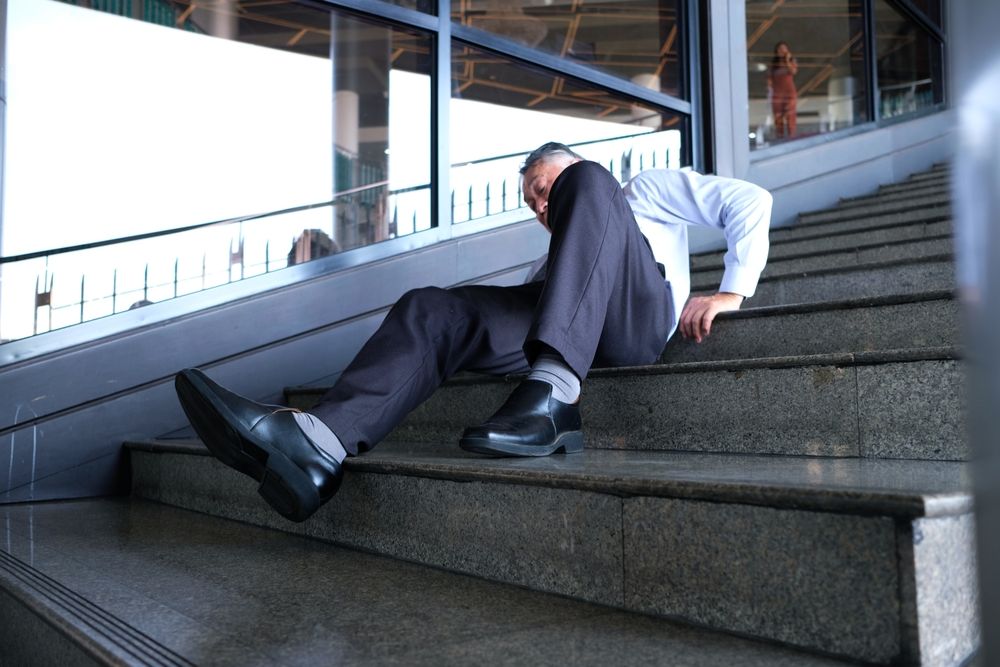 Man in a suit falling backward on concrete stairs, illustrating the sudden nature of slip and fall accidents on commercial property