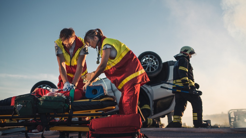 Paramedics treating a patient on a stretcher beside an overturned vehicle after a catastrophic injury accident